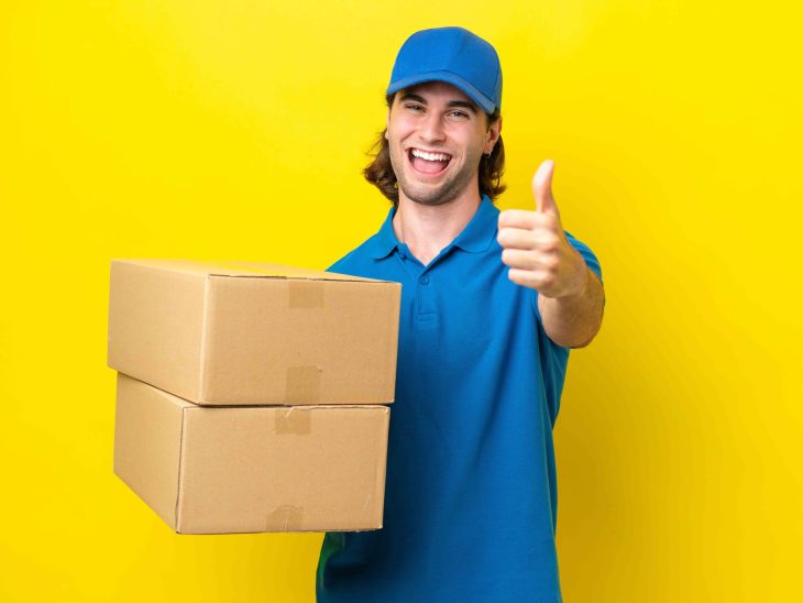 Delivery handsome man isolated on yellow background with thumbs up because something good has happened